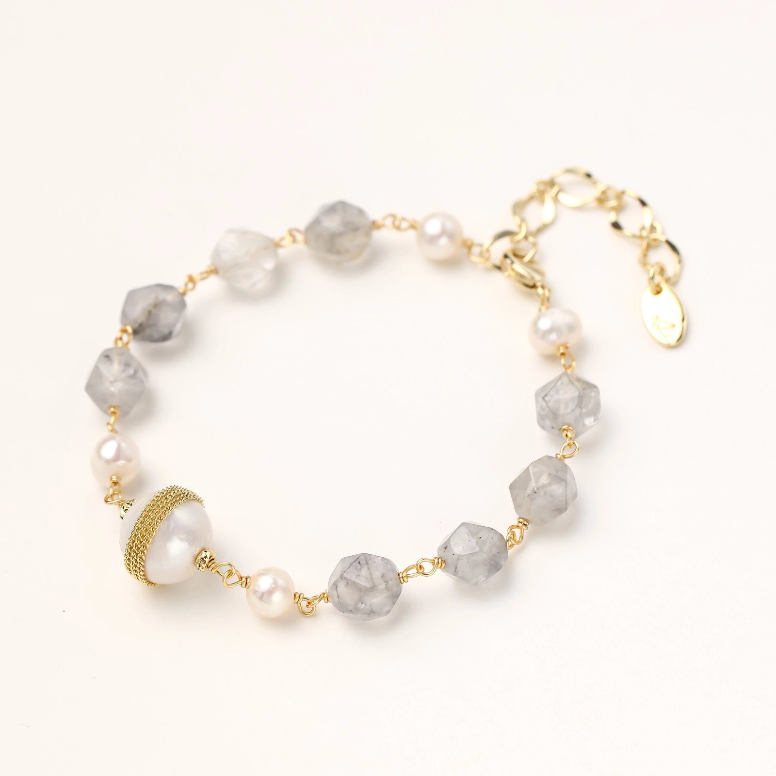 Bracelet with cloudy quartz beads, freshwater pearls, and gold-wrapped baroque pearl centerpiece on white background.