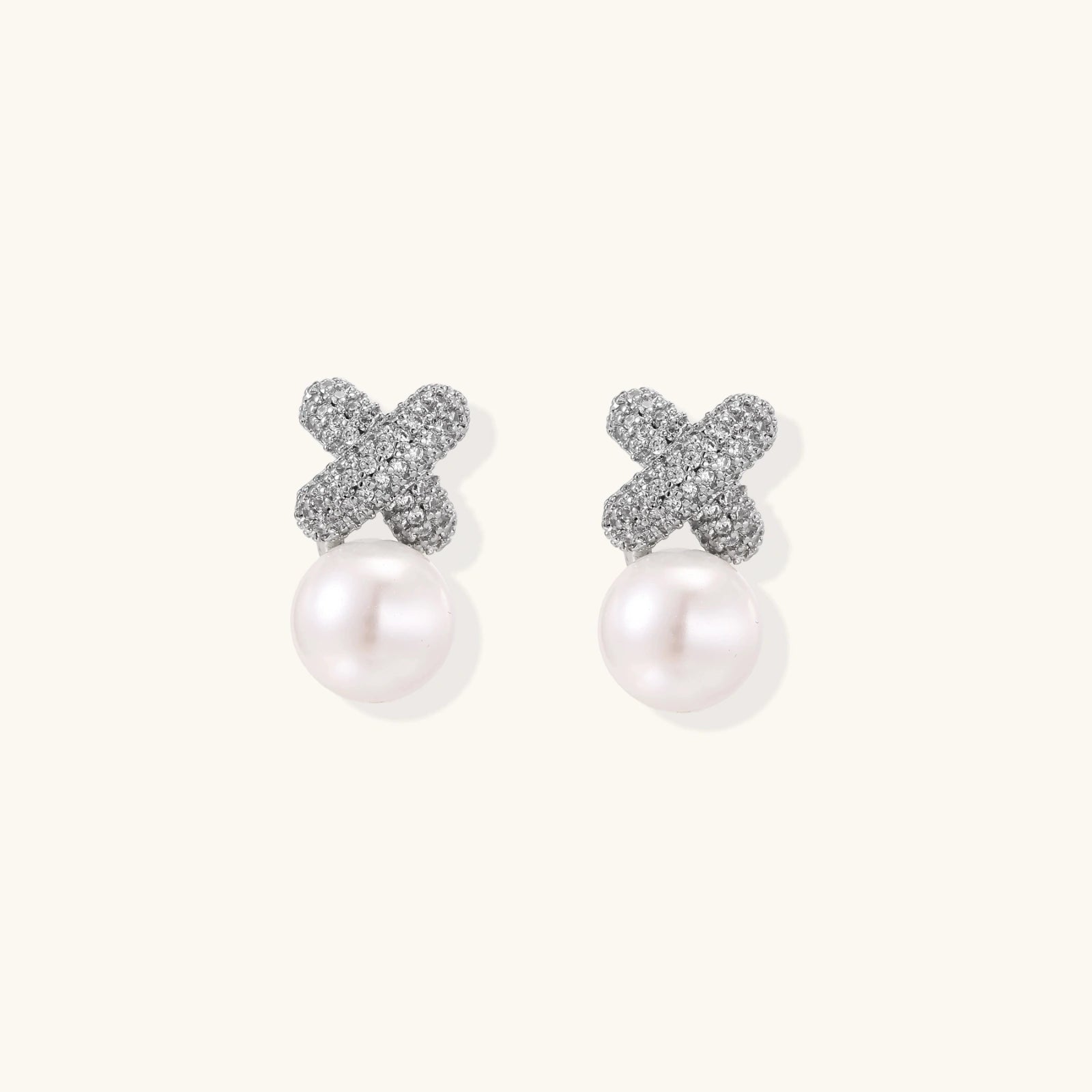White gold plated studs featuring pavé X-shaped tops with freshwater pearl drops on cream background.